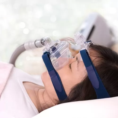 A woman asleep on her side wearing a CPAP nasal mask connected to a hose